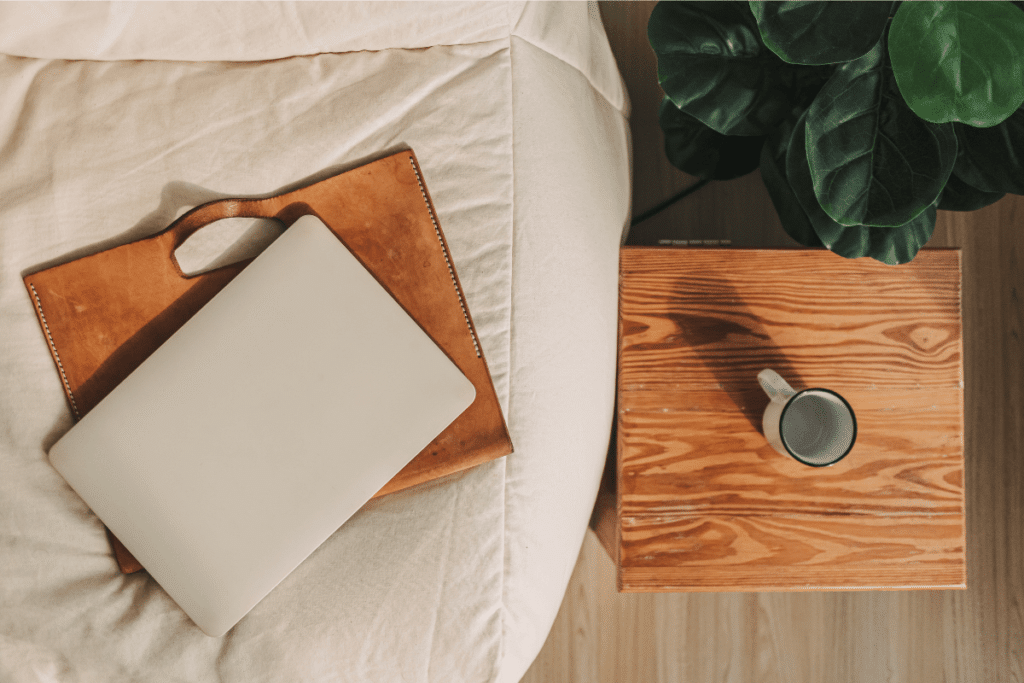 a laptop bag on a ottoman with a laptop on it, a coffee cup on a small table next to it
